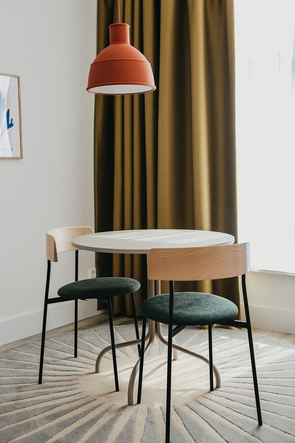 A dining area with a round table, two chairs, a red pendant light, and a patterned rug. - Hotel Bries Den Haag Scheveningen (The Hague)