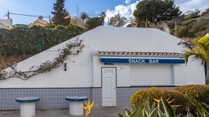 Ein weißes Gebäude mit einer blauen Markise, auf der 'SNACK BAR' steht, und eine Tür mit der Aufschrift 'LARA'.