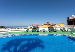 A pool with lounge chairs, a table with chairs, and a view of the sea.