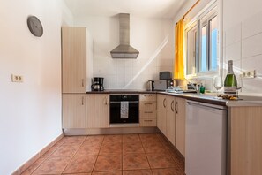 A kitchen with a stove, oven, and dishwasher, a window with curtains, and a clock on the wall.