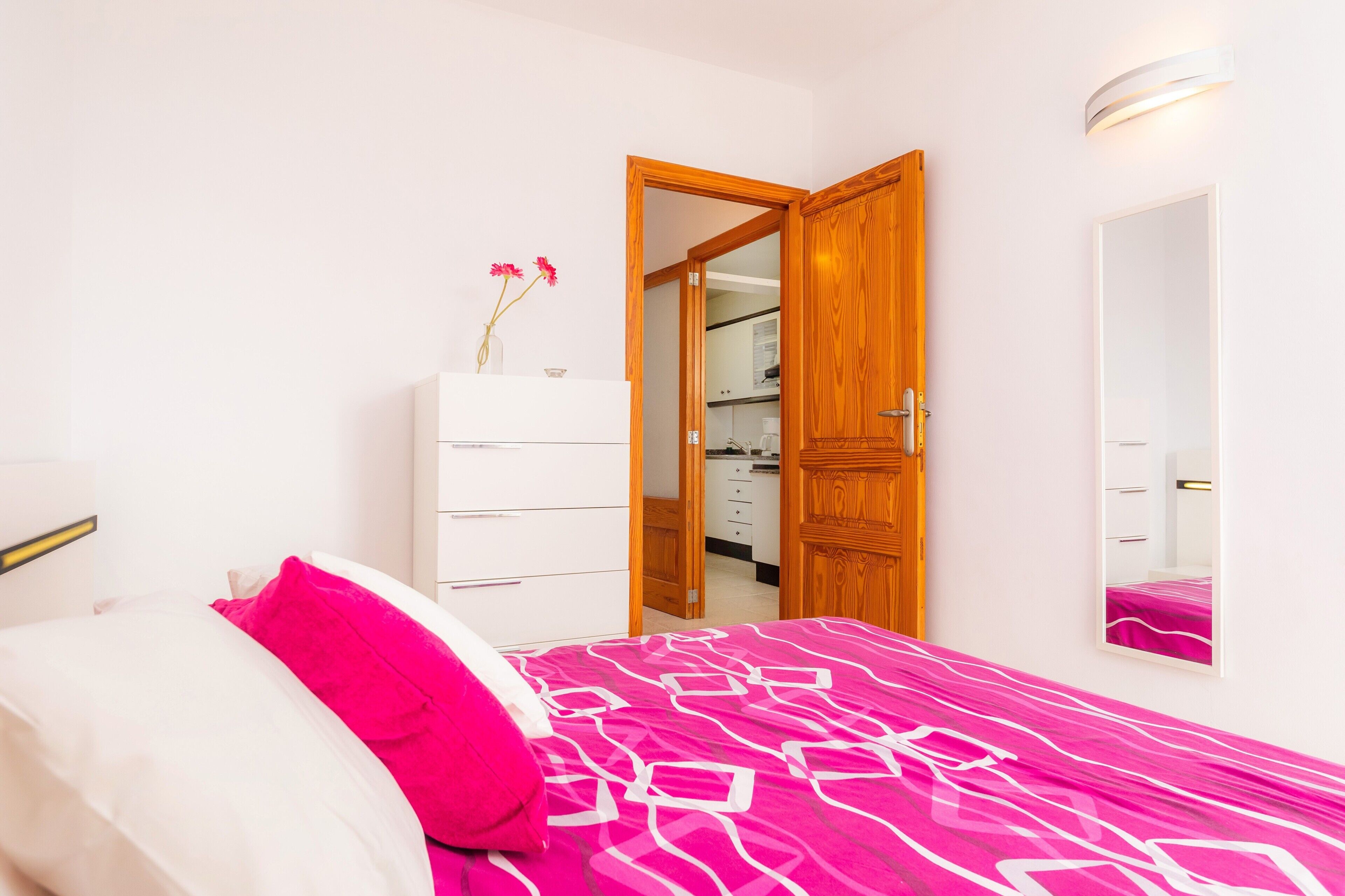 Una camera da letto con un letto, una cassettiera, uno specchio e una porta aperta che dà su un bagno.