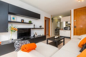A modern living room with a flat-screen TV, sofa, coffee table, and a kitchen in the background.