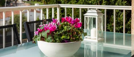 A glass table with a white bowl of pink flowers, a white lantern, and a black chair.