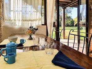 Una mesa de comedor con mantel amarillo, una jarra azul, dos tazas azules, un vaso y un cuenco con una planta.