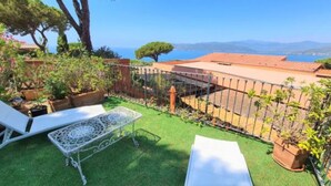 Un patio con mesa y sillas, un pequeño jardín y vistas al mar y las montañas.