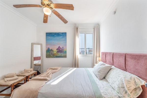 A bedroom with a bed, a ceiling fan, a window with curtains, a painting on the wall, and a bedside table with towels. - Casa Don Diego: Mountain Views, Wi-Fi, and Air Conditioning (Ardales)