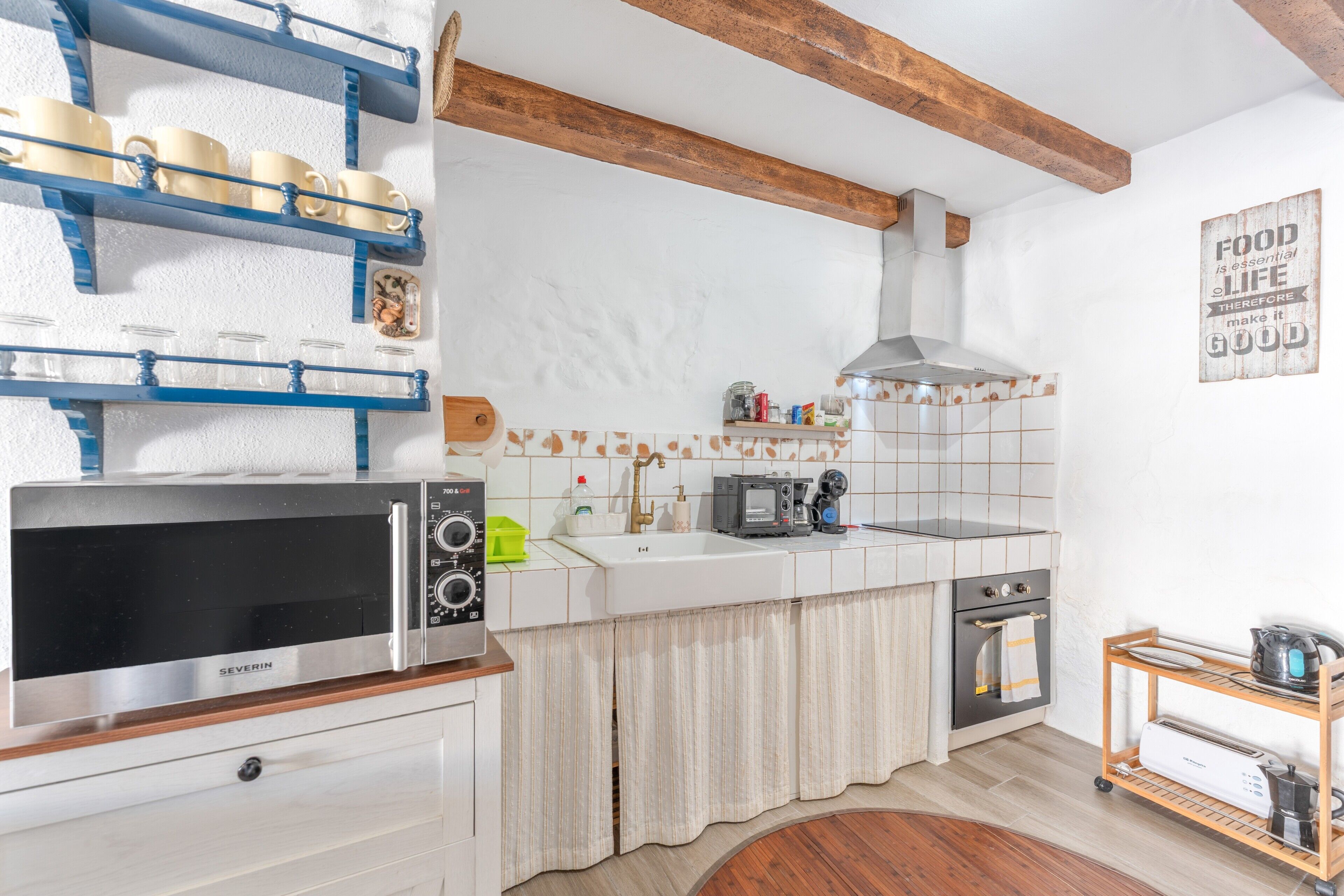 A kitchen with a microwave, oven, sink, and a wooden shelf with cups.