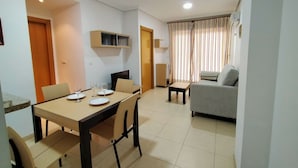 Un comedor con una mesa preparada para cuatro, un sofá y un televisor montado en la pared.