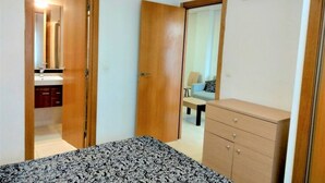 Ein Schlafzimmer mit einem Bett, einer Kommode, einer offenen Tür zu einem Badezimmer und einer Klimaanlage an der Wand.