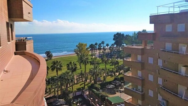 Un immeuble de grande hauteur doté de balcons donnant sur une plage et des palmiers.