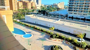 A hotel with a swimming pool, a parking area, and a view of the cityscape.
