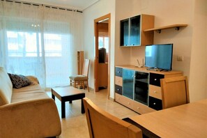 Una sala moderna con un sofá, una mesa de centro, un televisor sobre un mueble de madera y un comedor con una mesa y sillas.