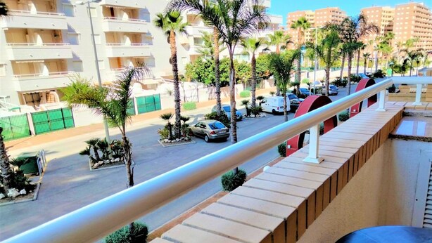 A balcony with a view of a parking lot, palm trees, and a building with balconies.