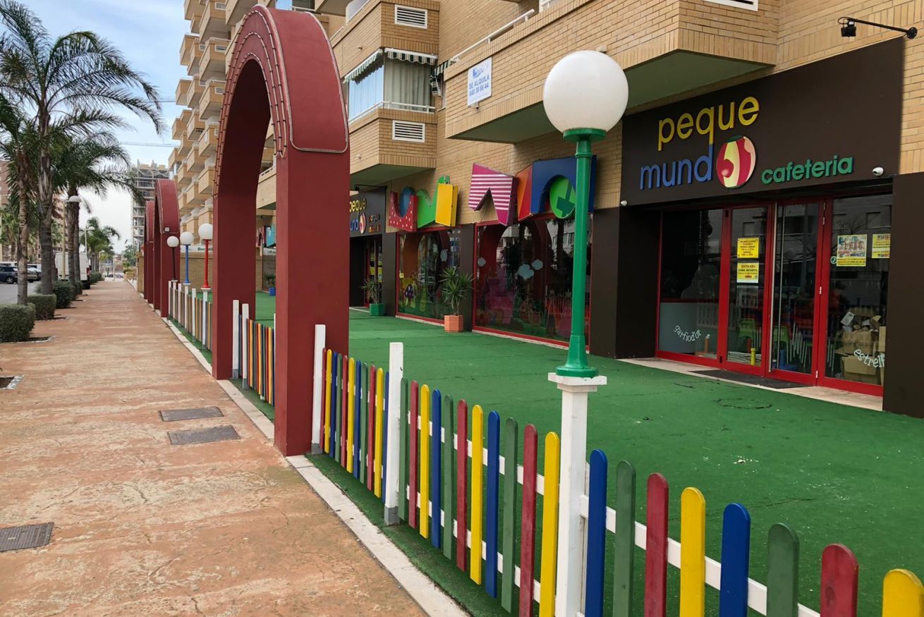 A colorful pedestrian walkway with a green surface, bordered by a multicolored fence, and adjacent buildings with commercial establishments.