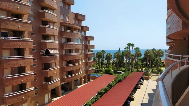 Un hotel de varios pisos con balcones, una pista de atletismo roja y vista al mar.