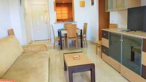 A compact living space with a sofa, a small table, a dining area with chairs, and a kitchenette with cabinets and a TV.