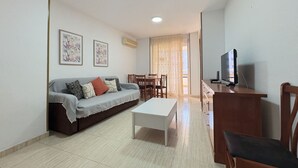 Un salon comprenant un canapé, une table basse, un téléviseur et un coin repas avec des chaises et une table.