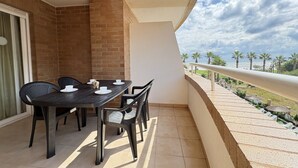 Un balcon avec une table et des chaises, une vue sur les palmiers et la mer, et un mur en briques.