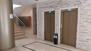 Un hall d’entrée avec un mur en pierre, deux ascenseurs, une poubelle et un escalier.