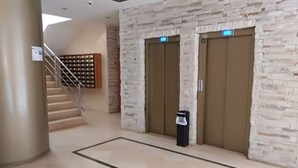 Un vestíbulo con pared de piedra, dos ascensores, un cesto de basura y una escalera.