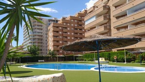 A swimming pool with a mosaic edge, surrounded by green artificial turf, and a palm tree in the foreground.