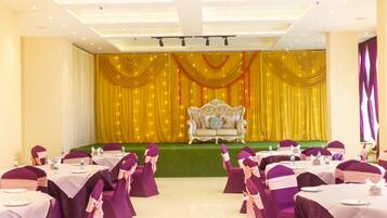 Een feestzaal met gedekte tafels voor een formeel evenement, een podium met gouden gordijnen en een luxe bank.