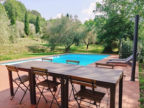 A swimming pool with a wooden deck, lounge chairs, and a table. - 3 bedroom apartment in Tuscan farmhouse with private pool & game room | 8 guests (Reggello)