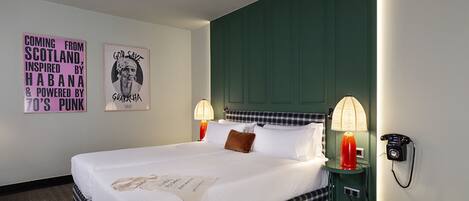 Una habitación de hotel con una cama grande, dos lámparas de noche, un teléfono y dos obras de arte en la pared.