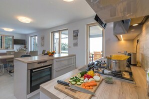 A modern kitchen with a central island, an oven, a stove, and a dining area with chairs and a table.