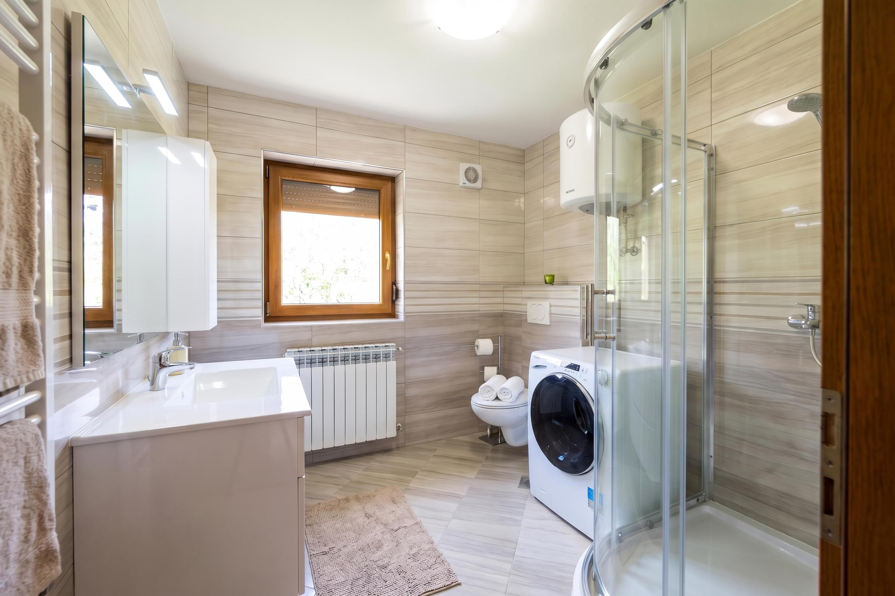 A modern bathroom with a glass shower enclosure, a built-in washing machine, and a radiator.
