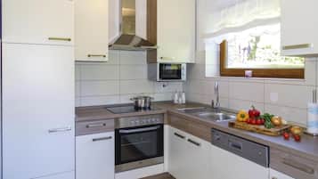A modern kitchen with white cabinetry, a built-in oven, a microwave, and a window with a view of greenery.