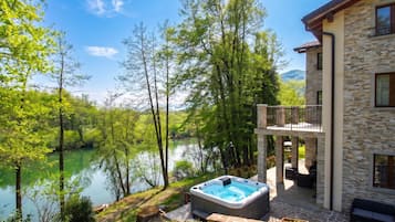 A house with a hot tub, a balcony, and a view of a lake surrounded by trees.