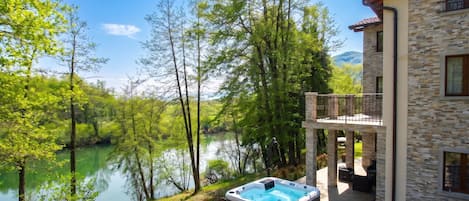 A house with a hot tub, a balcony, and a view of a lake surrounded by trees.