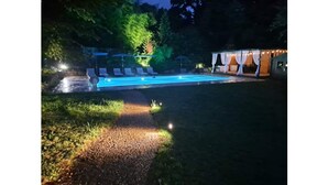 A swimming pool with lounge chairs and a covered area, surrounded by trees and a gravel path. - Peaceful Gite in the heart of the Perigord Noir (Mauzens-et-Miremont)