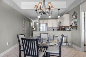 A dining area with a round glass table, four chairs, and a chandelier. - The Whart Unit 505 2 Bedroom Condo by RedAwning (Orange Beach)
