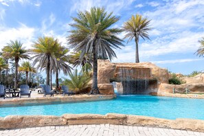 A swimming pool with palm trees and a waterfall feature. - The Whart Unit 505 2 Bedroom Condo by RedAwning (Orange Beach)