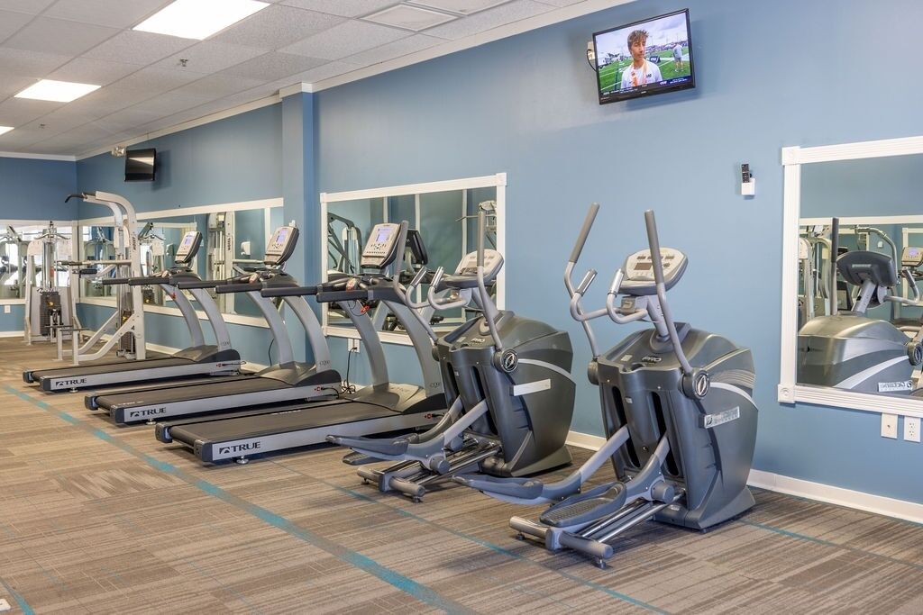 A gym with multiple treadmills and elliptical machines, a TV on the wall, and mirrors on the walls.