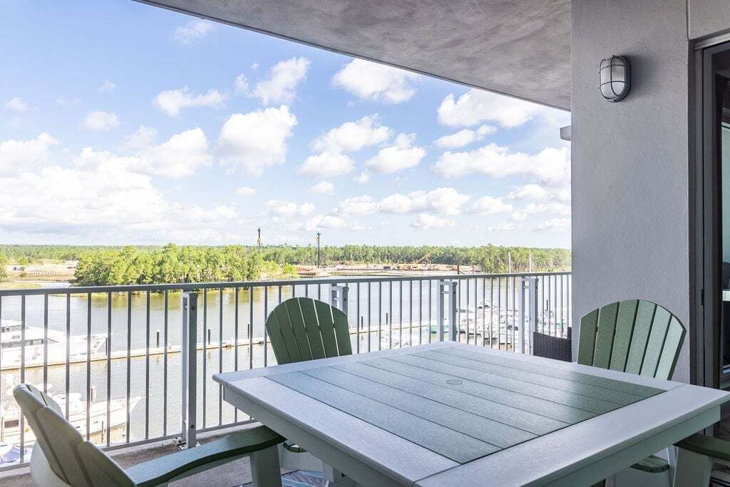 A balcony with a table and chairs, overlooking a body of water and greenery.