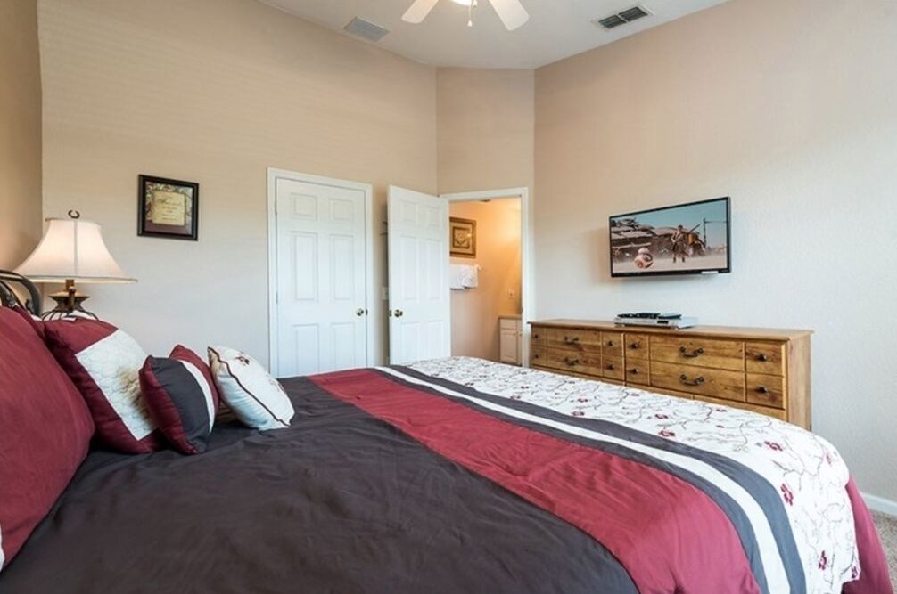 A bedroom with a bed, a dresser, a lamp, and a television on the wall.