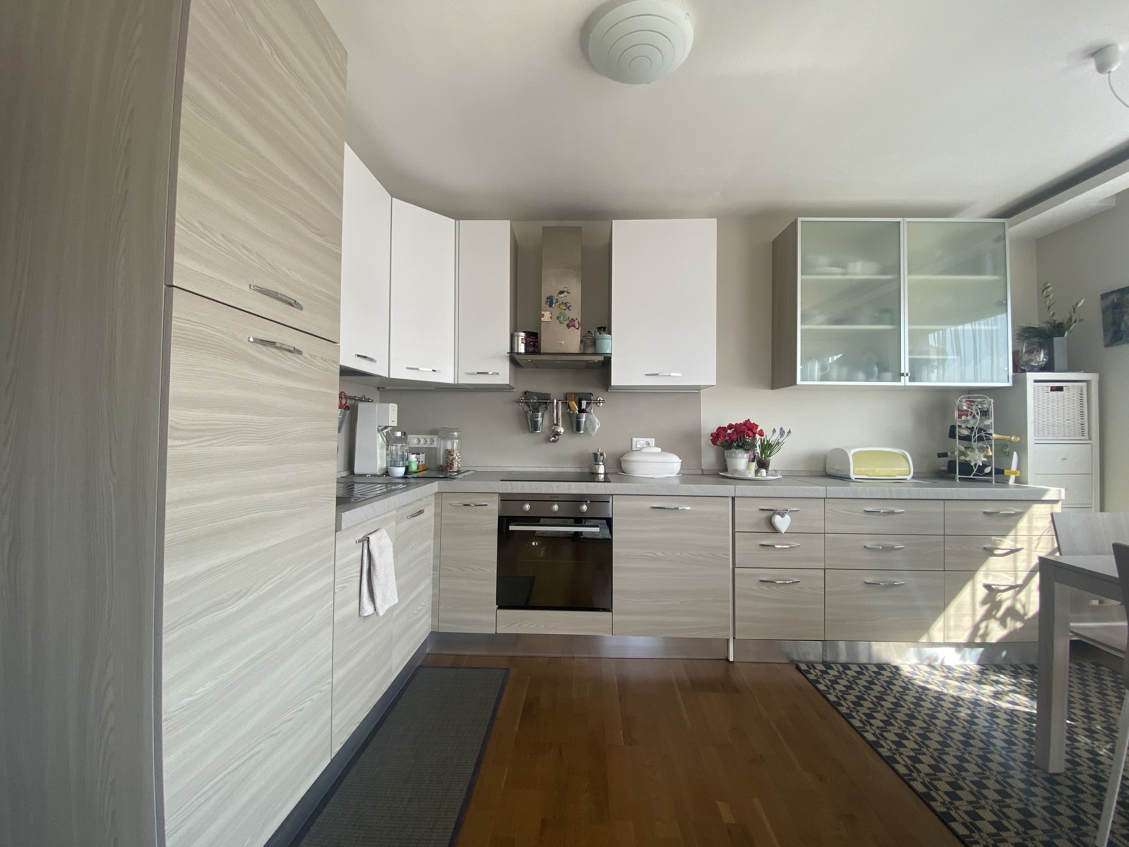 A modern kitchen with light wood cabinetry, a built-in oven, and a stainless steel sink.
