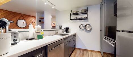 A modern kitchen with stainless steel appliances, a white countertop, and wooden flooring.