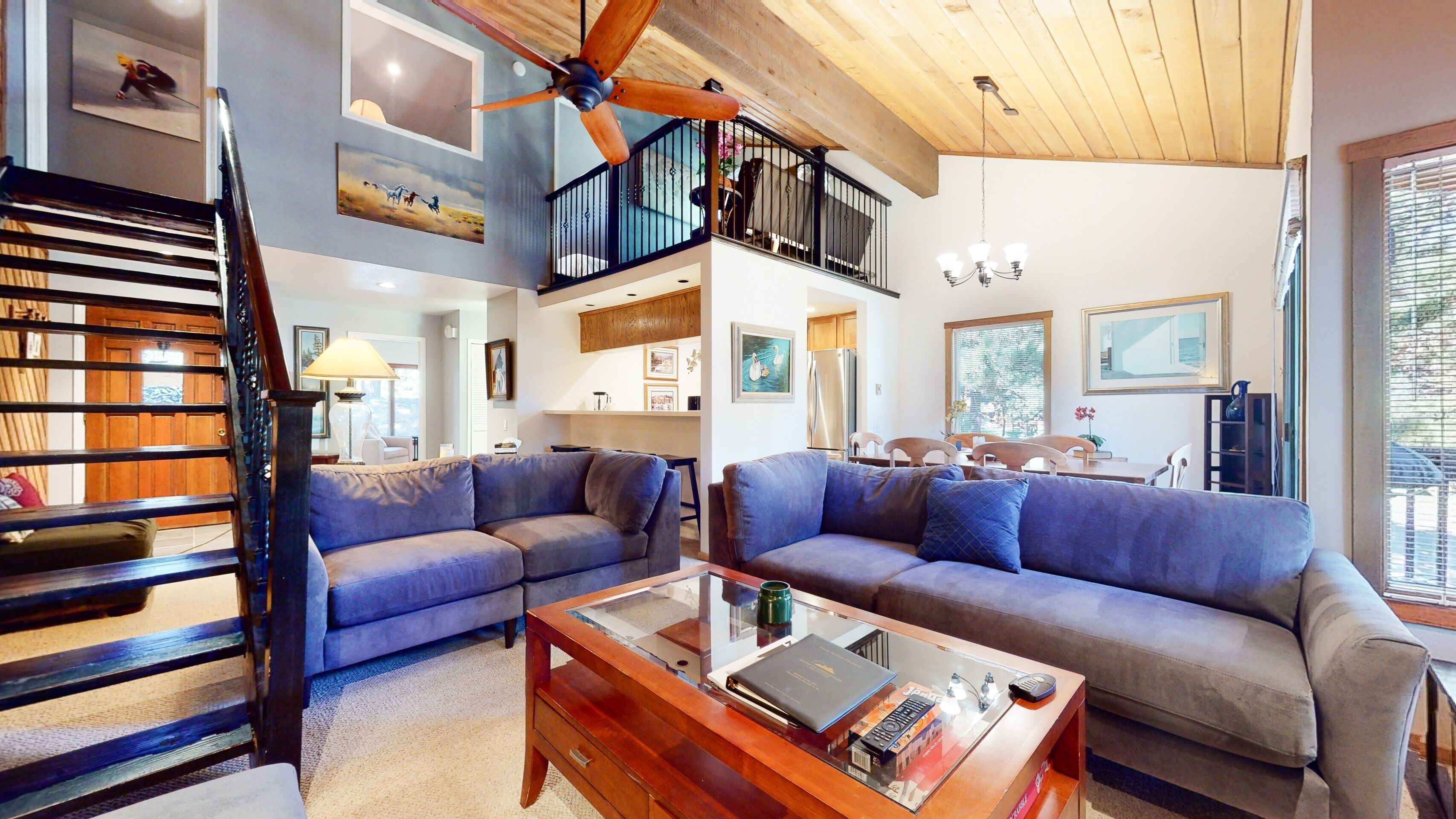 A spacious living area with a high ceiling, a wooden staircase, and a dining area with a view of the outdoors.