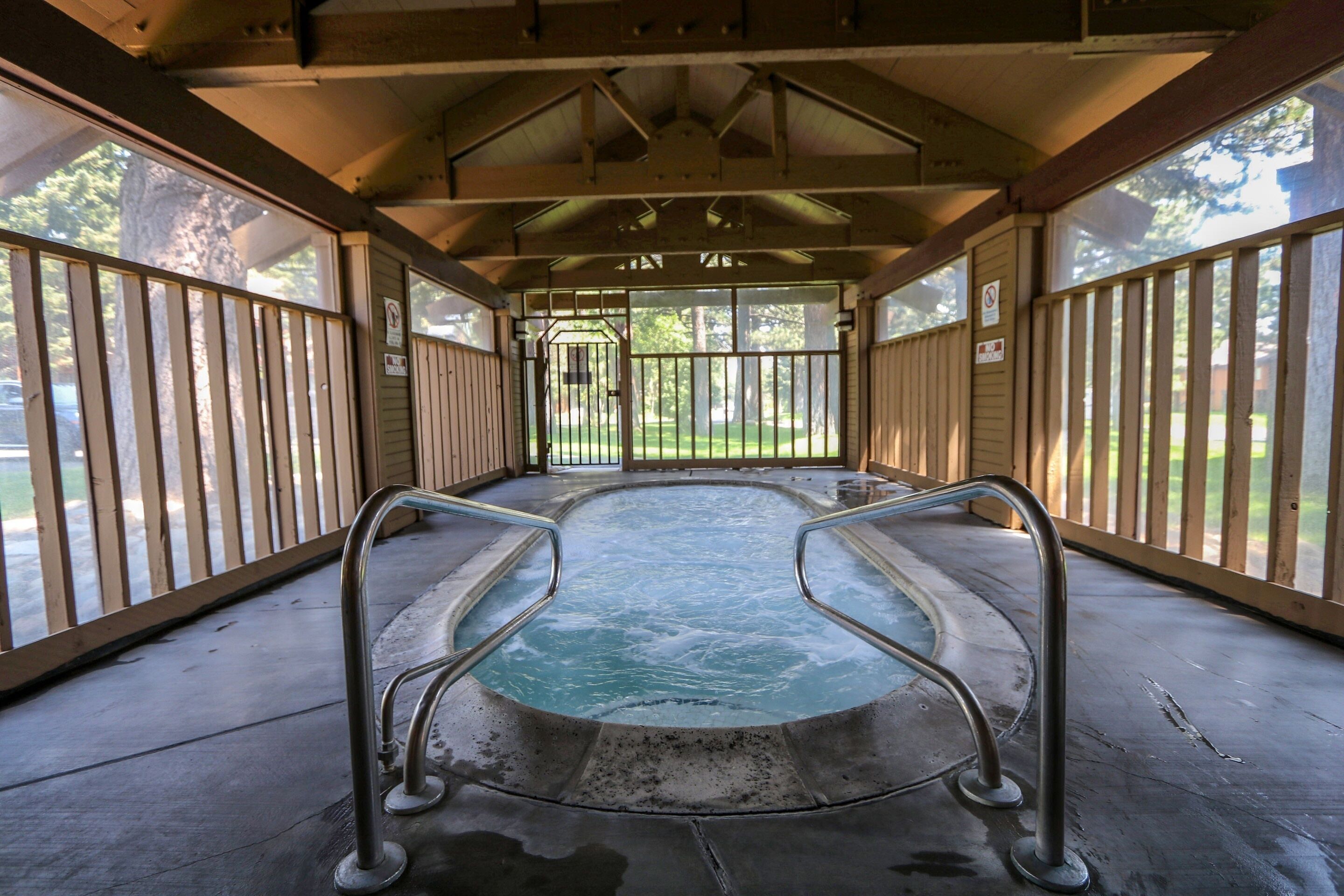 An indoor hot tub with metal railings, a concrete floor, and a wooden ceiling.
