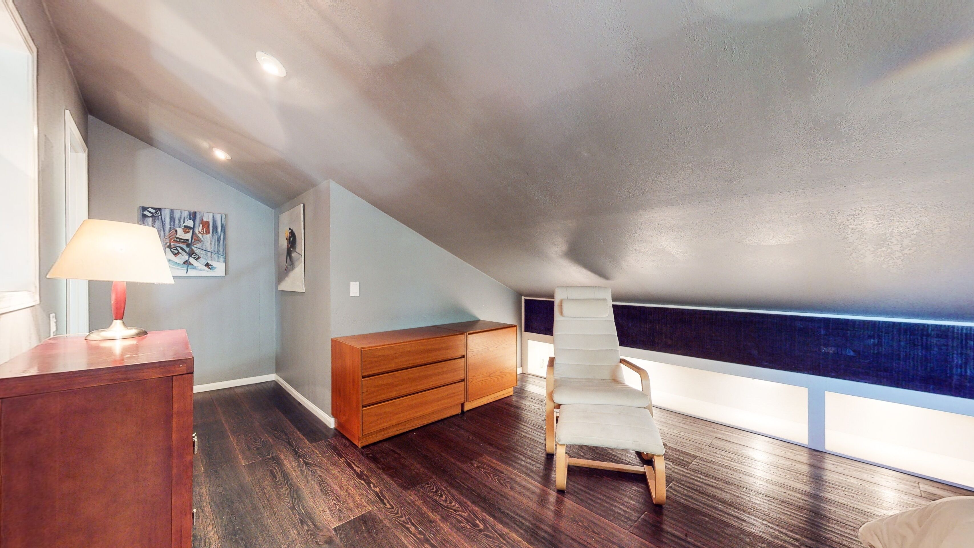 Une pièce avec un plafond en pente, une commode en bois, une chaise blanche et une fenêtre donnant sur un beau paysage.