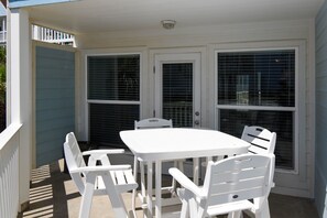 A covered patio area with a white table and four chairs, a door with a window, and a light fixture above the door.