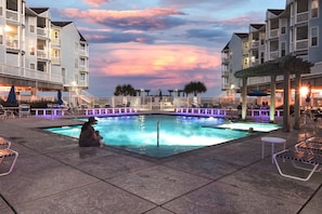 A pool area with a woman and child, surrounded by buildings with balconies and outdoor seating.