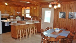 Cocina de estilo cabaña de madera con una isla central, taburetes de bar y una mesa de comedor con sillas.