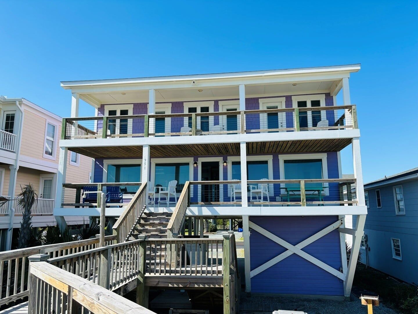Un edificio de varios pisos frente a la playa con un muelle de madera y escaleras que conducen a los niveles superiores.