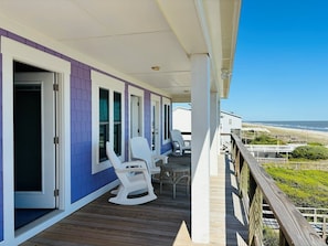 A covered porch with white rocking chairs and a wooden deck, overlooking a beach. - Nothin But Nett 5 Bedroom Home by RedAwning (Supply)