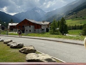 A rustic mountain lodge with a stone facade, a wooden roof, and a view of snow-capped mountains in the background.